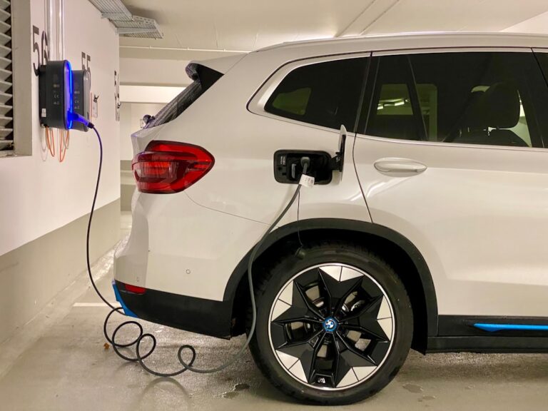 Förderungen und Förderprogramme für Wallboxen in Mehrfamilienhäusern nutzen Wallbox-Ladestation in Mehrfamilienhaus mit Förderhinweisen und E-Auto im Hintergrund